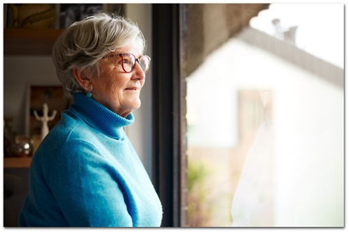 Ældre kvinde med blå sweater kigger ud ad vindue